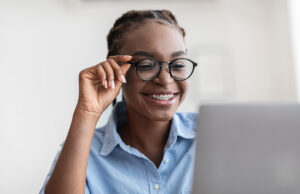 Young Specialist. Smiling lady with stylish eyeglasses and braces using laptop at workplace in office, working on computer, looking at screen and smiling, closeup shot, free space