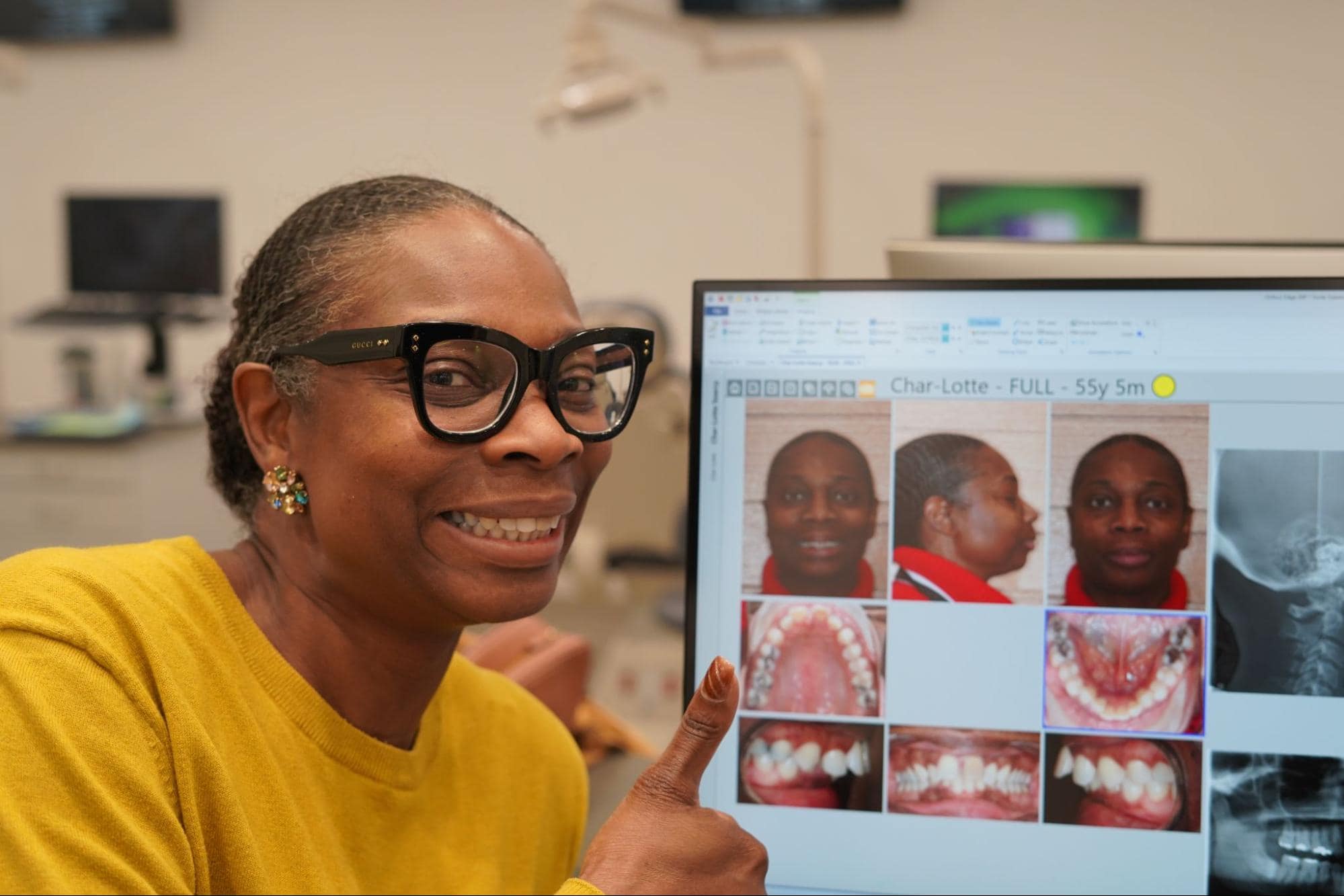 A smiling patient giving a thumbs up next to a screen displaying her dental records.